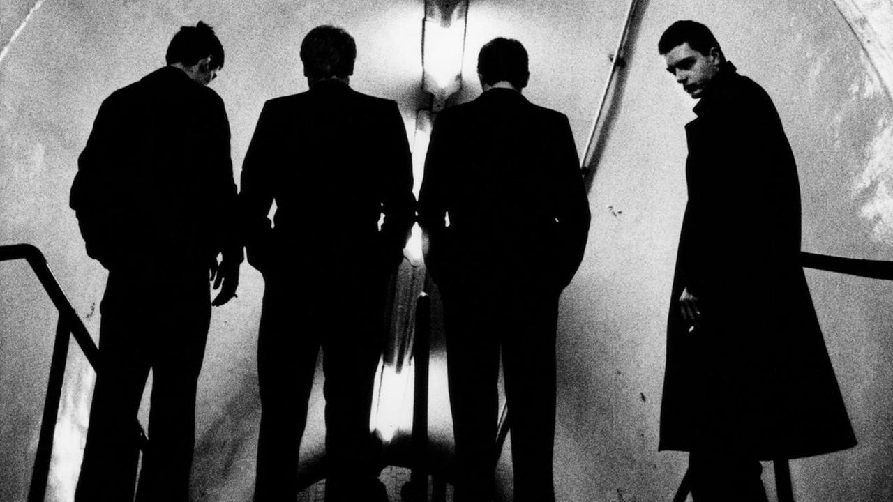 Eine Schwarz-weiß-Aufnahme des Fotografen Anton Corbijn ziegt die Band Joy Division beim Abstieg in die U-Bahn Eine Schwarz-weiß-Aufnahme des Fotografen Anton Corbijn ziegt die Band Joy Division beim Abstieg in die U-Bahn
