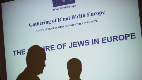 Zwei Schatten sind vor einer Leinwand zu sehen, auf der steht: "Die Zukunft der Juden in Europa"