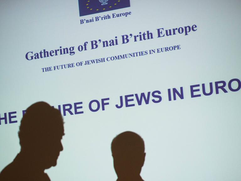 Zwei Schatten sind vor einer Leinwand zu sehen, auf der steht: "Die Zukunft der Juden in Europa"