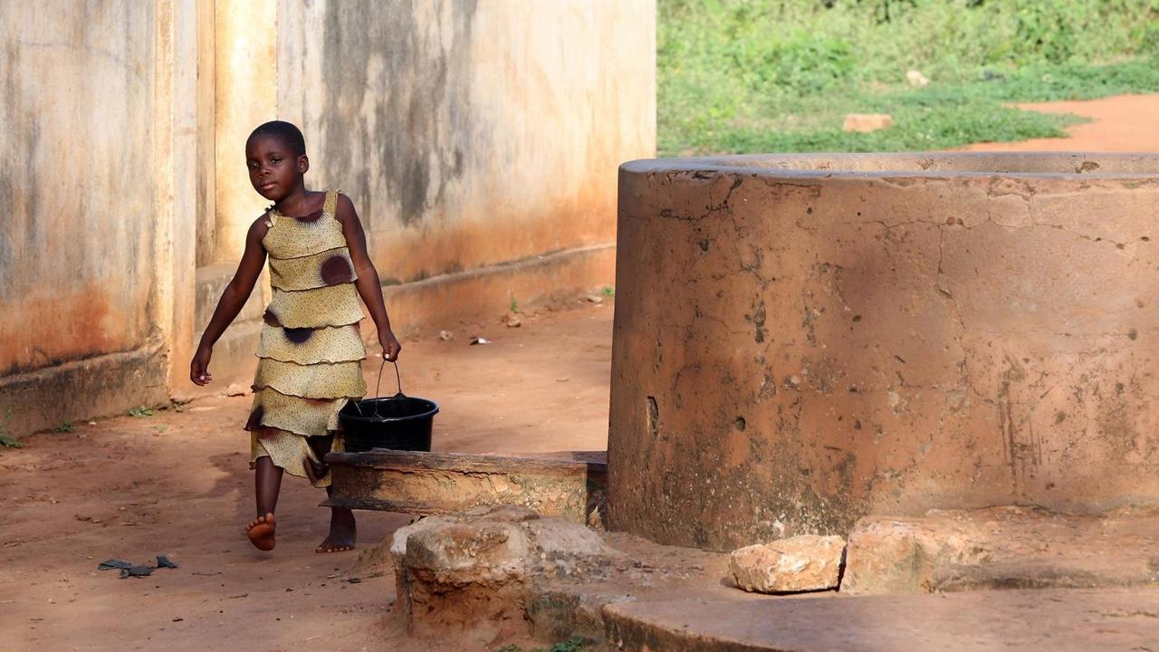 Ein Mädchen trägt einen Wassereimer in einem Dorf in Togo, Afrika. Ein Mädchen trägt einen Wassereimer in einem Dorf in Togo, Afrika.