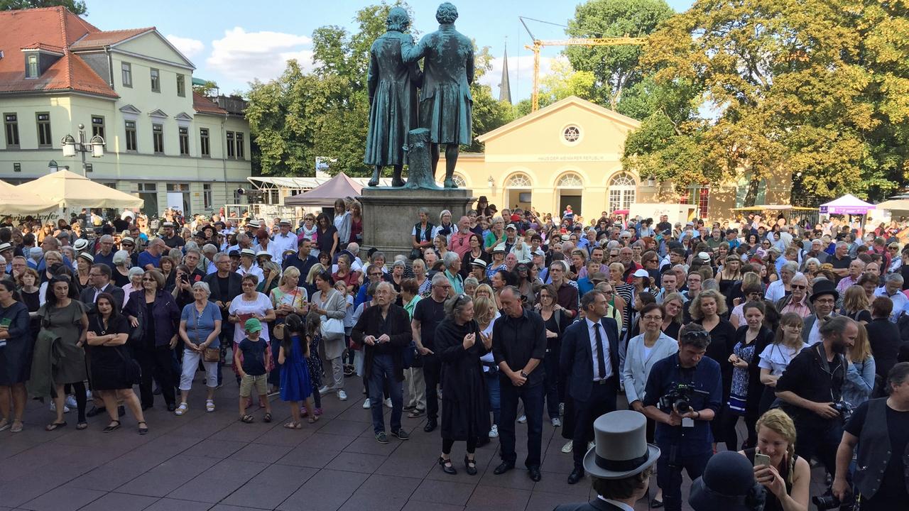 Eine Menschengruppe steht auf dem Platz mit dem Goethe- und Schiller-Denkmal auf dem Theaterplatz in Weimar.