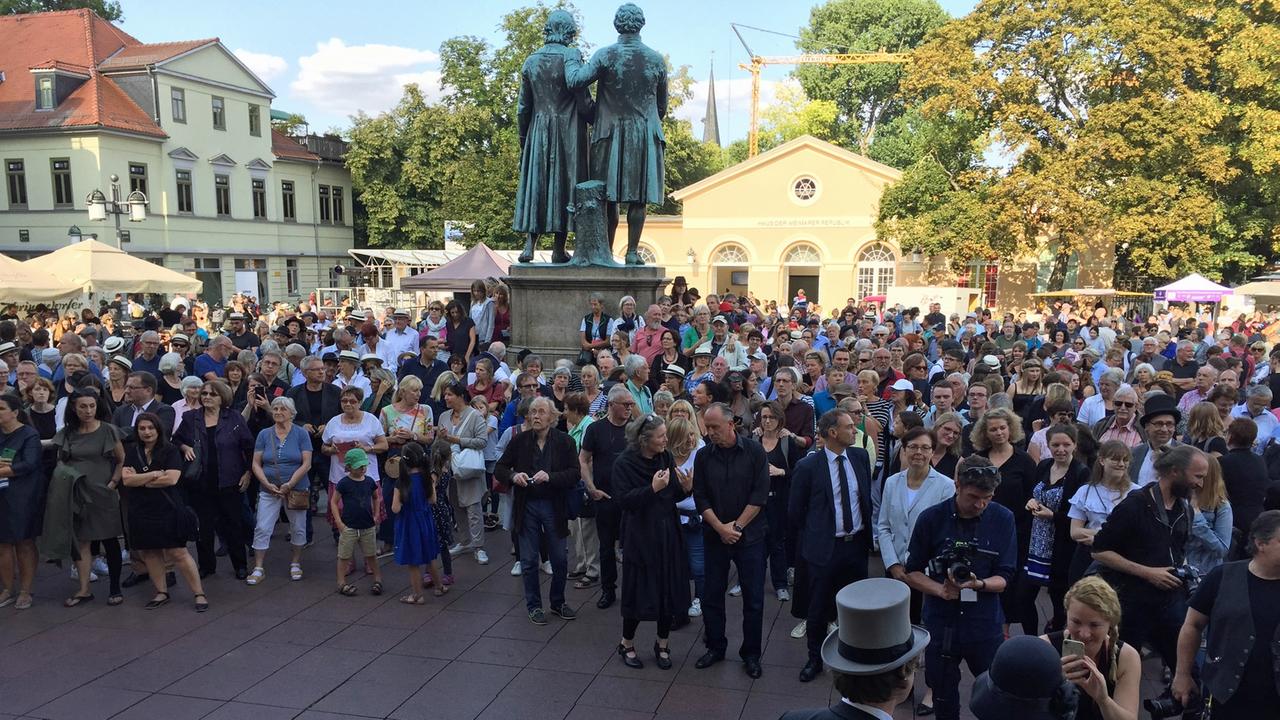 Eine Menschengruppe steht auf dem Platz mit dem Goethe- und Schiller-Denkmal auf dem Theaterplatz in Weimar. Eine Menschengruppe steht auf dem Platz mit dem Goethe- und Schiller-Denkmal auf dem Theaterplatz in Weimar.