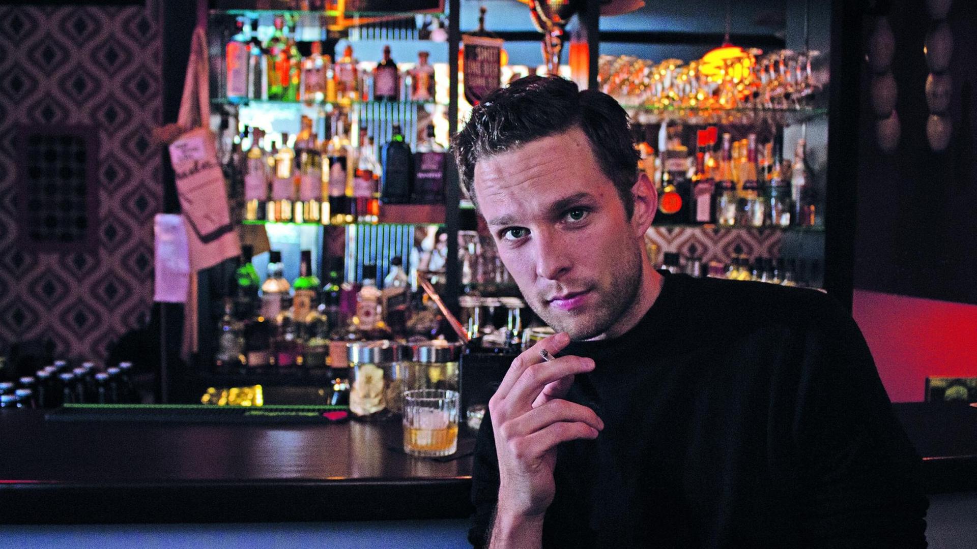 Die Szene aus dem Stück "Sieben Nächte" zeigt einen rauchenden Mann an einer Bar.