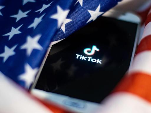 Handy mit TikTok-Logo auf dem Display versinkt in US-Flagge