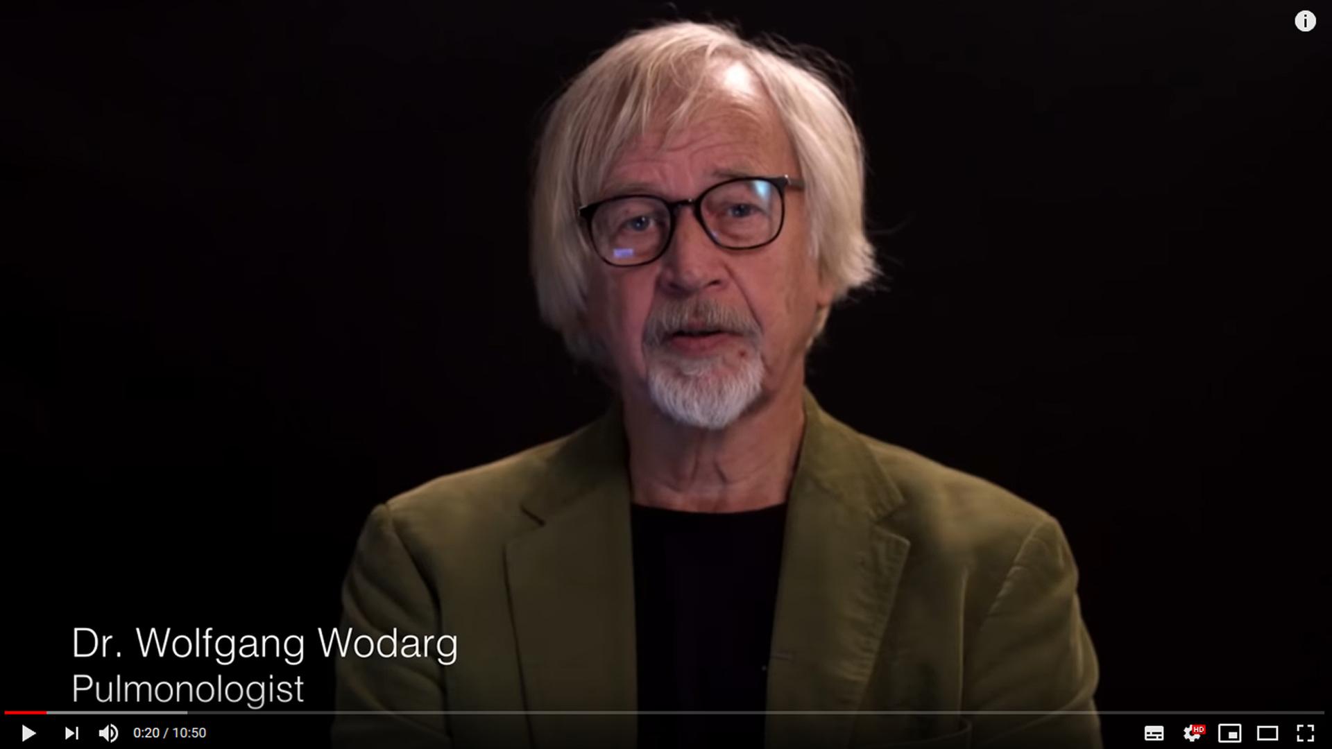 Der Lungenarzt Wolfgang Wodarg in einem Video. Ein Mann mit grauen Haaren und Bart sitzt vor einem schwarzen Hintergrund und schaut in eine Kamera. Der Lungenarzt Wolfgang Wodarg in einem Video. Ein Mann mit grauen Haaren und Bart sitzt vor einem schwarzen Hintergrund und schaut in eine Kamera.