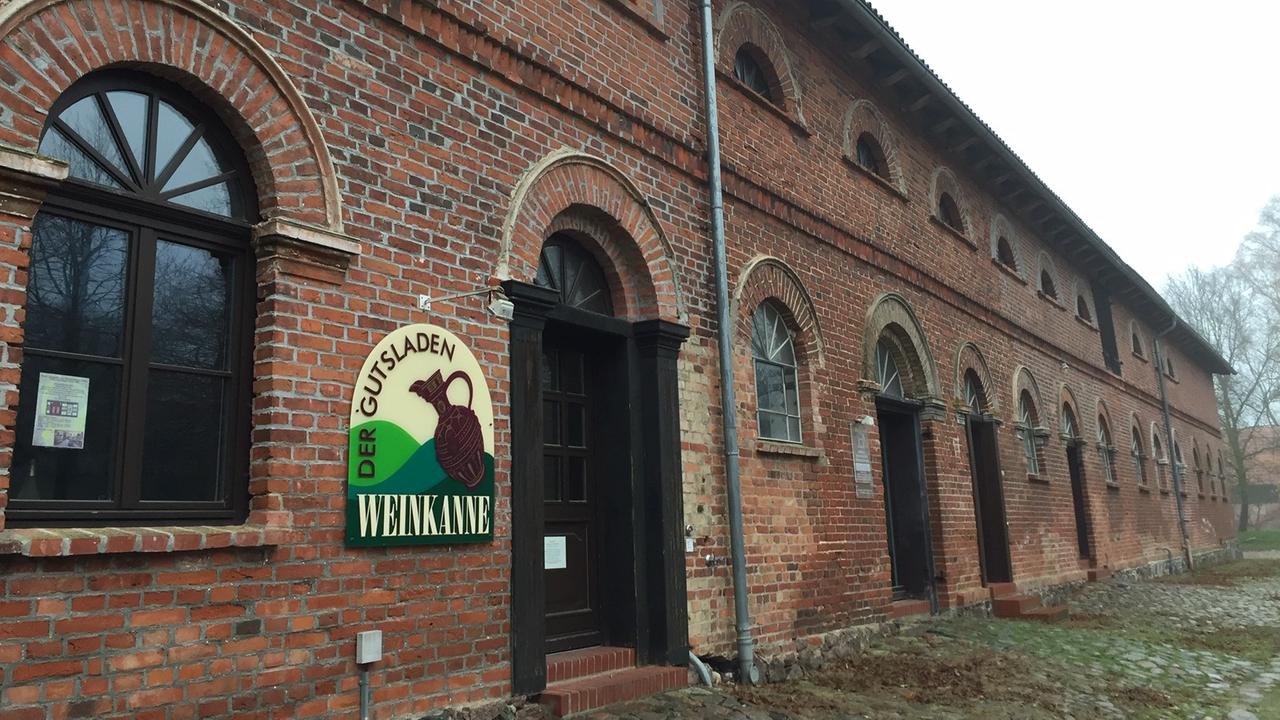 Das Bild zeigt ein langes rotes Backsteingebäude, an dessen Tür ein Schild mit der Aufschrift "Gutsladen" hängt. Das Bild zeigt ein langes rotes Backsteingebäude, an dessen Tür ein Schild mit der Aufschrift "Gutsladen" hängt.