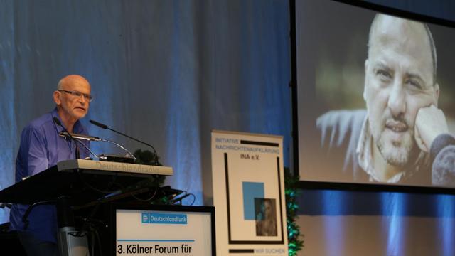 Laudator Günter Wallraff beim 3. Kölner Forum für Journalismuskritik, im Hintergrund ein Foto von Preisträger Ahmet Şık