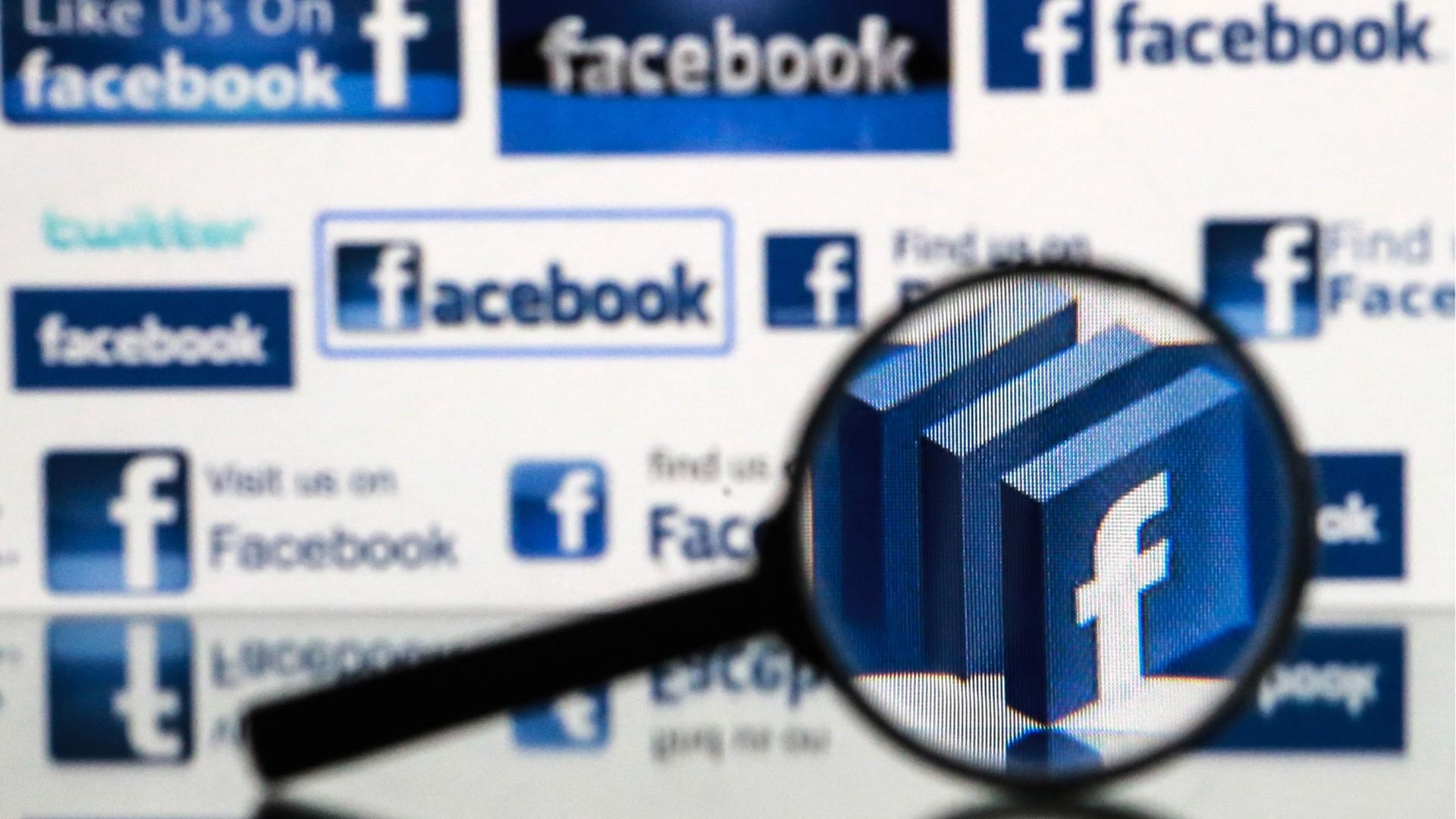 Eine Lupe vor einem Computer-Bildschirm mit Facebook-Logo. Eine Lupe vor einem Computer-Bildschirm mit Facebook-Logo.