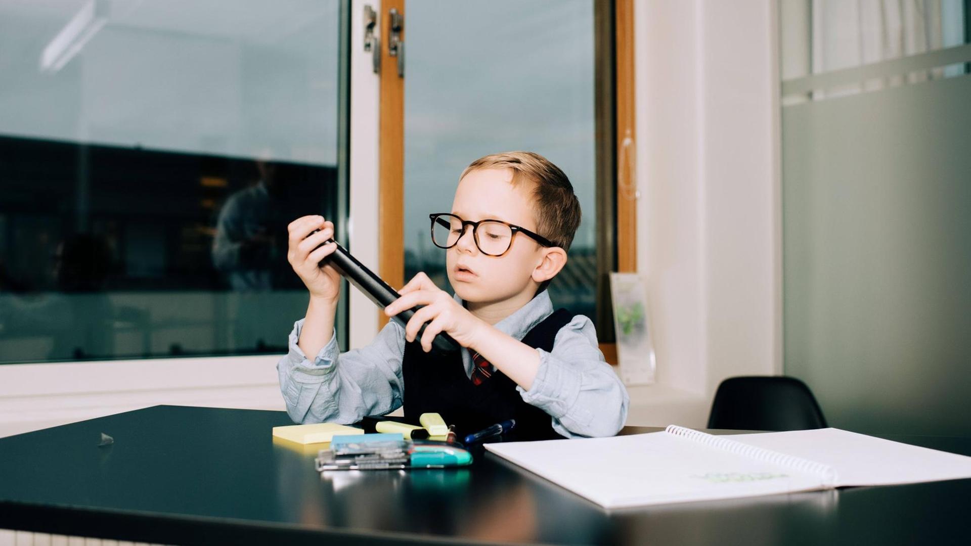 Ein Junge sitzt im Büro an einem Schreibtisch und sortiert Stifte. Ein Junge sitzt im Büro an einem Schreibtisch und sortiert Stifte.