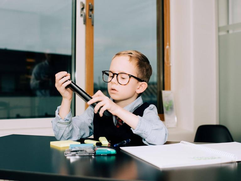 Ein Junge sitzt im Büro an einem Schreibtisch und sortiert Stifte.