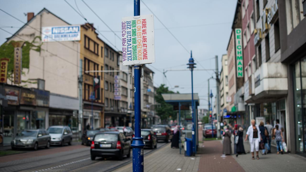 Ein Schild "Hier sind wir zuhause" in verschiedenen Sprachen hängt am 12.08.2015 in Duisburg (Nordrhein-Westfalen) auf der Straße. Händlern brechen die Geschäfte weg, Familienclans reklamieren die Gegend für sich. Ein Schild "Hier sind wir zuhause" in verschiedenen Sprachen hängt am 12.08.2015 in Duisburg (Nordrhein-Westfalen) auf der Straße. Händlern brechen die Geschäfte weg, Familienclans reklamieren die Gegend für sich.