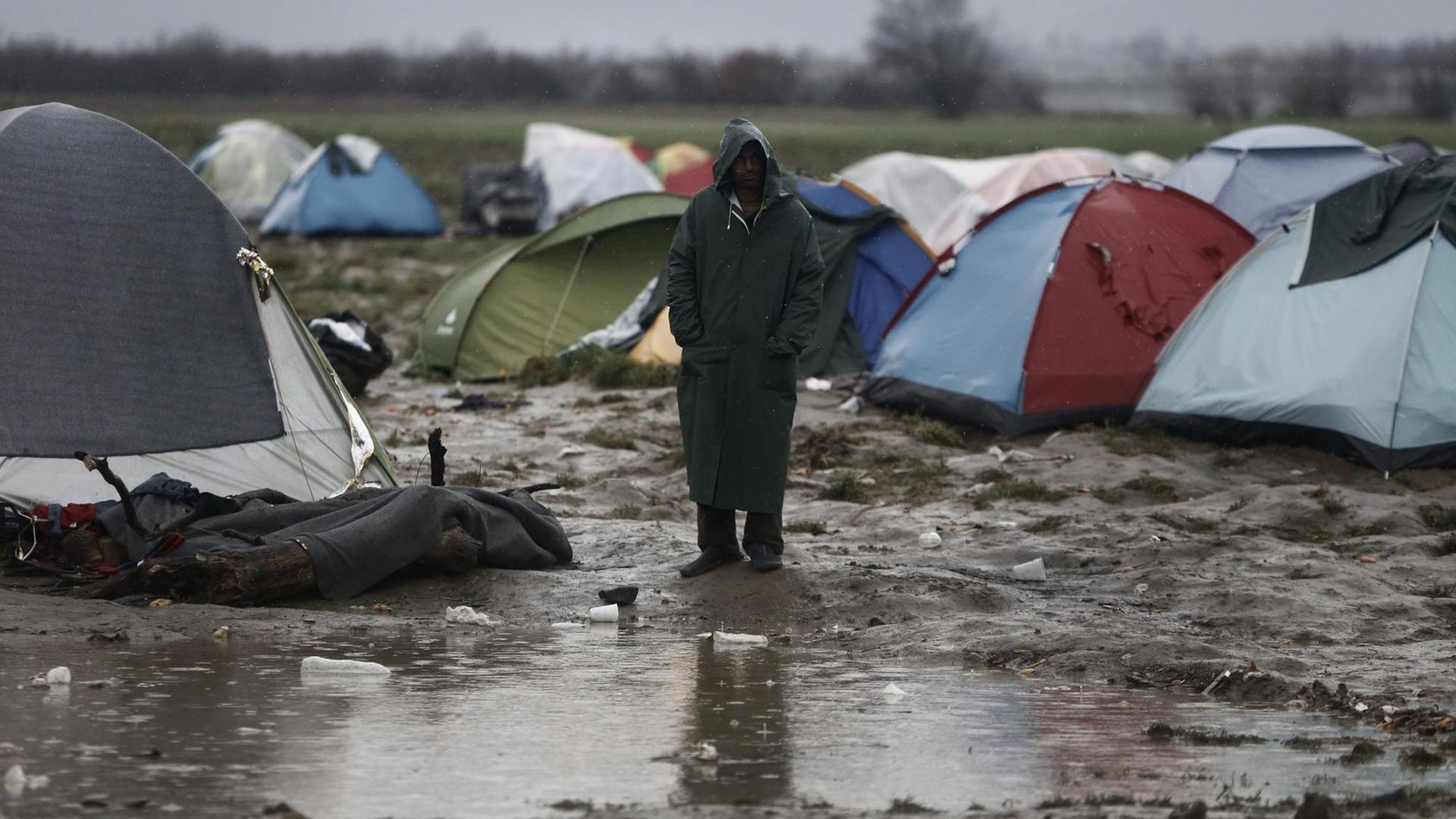 Ein Mann steht vor einer Gruppe von Campingzelten im Regen, vor ihm eine große Pfütze. Ein Mann steht vor einer Gruppe von Campingzelten im Regen, vor ihm eine große Pfütze.