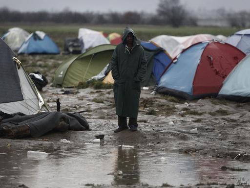 Ein Mann steht vor einer Gruppe von Campingzelten im Regen, vor ihm eine große Pfütze.