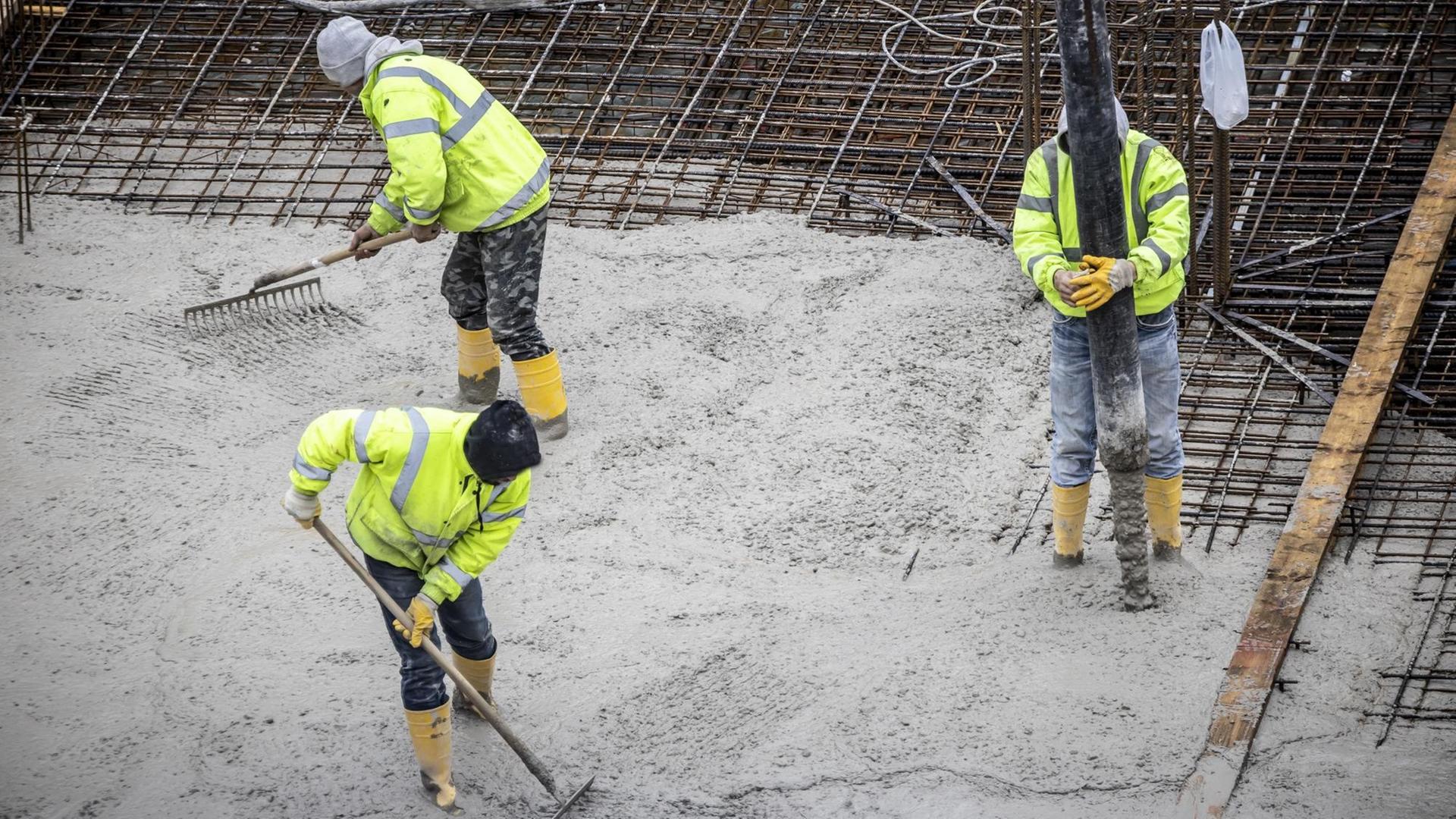 Drei Bauaerbeiter bei der Arbeit. Das Fundament eine Gebäudes wird betoniert, der Beton kommt per Betonpumpe auf die Stahlbeton-Matten. Drei Bauaerbeiter bei der Arbeit. Das Fundament eine Gebäudes wird betoniert, der Beton kommt per Betonpumpe auf die Stahlbeton-Matten.