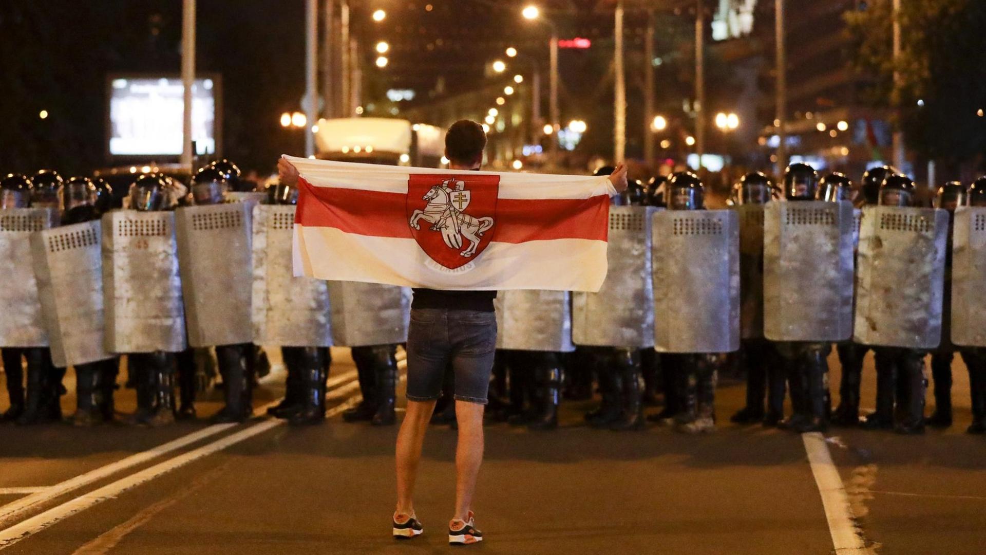 Ein Demonstrant hält die belarussische Flagge vor der versammelten Polizei. Ein Demonstrant hält die belarussische Flagge vor der versammelten Polizei.