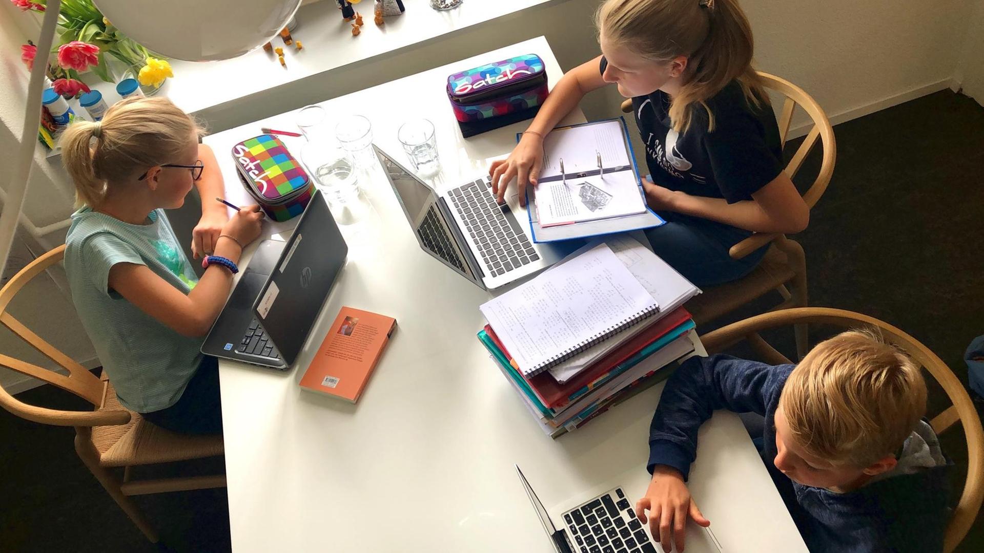 Drei Kinder sitzen mit Laptops an einem Tisch Drei Kinder sitzen mit Laptops an einem Tisch