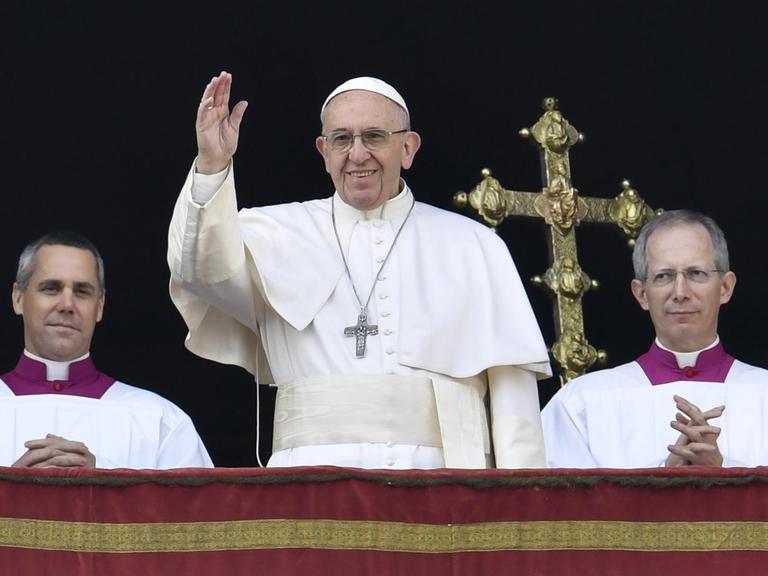 Papst Franziskus und zwei weitere Männer stehen auf dem Balkon des Petersdoms.