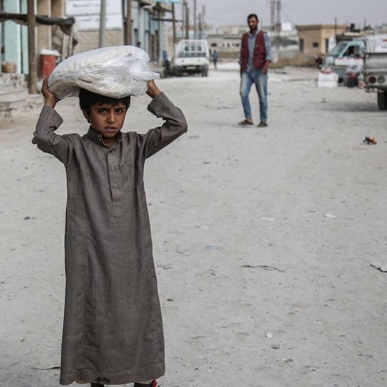 Ein syrischer Junge trägt auf einer Straße Essen auf seinem Kopf. 