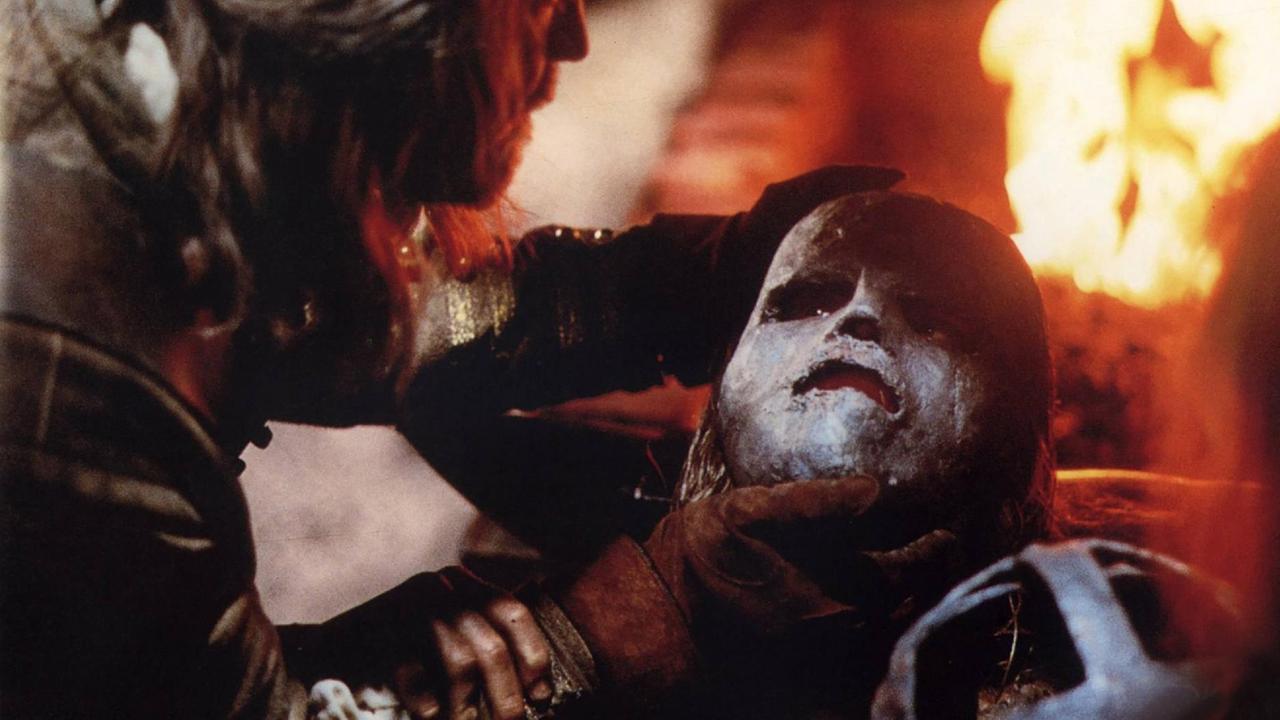 Ein Mann hält eine eiserne Maske über das Gesicht eines anderen Mannes. Dahiner ist ein Feuer zu sehen. Ein Mann hält eine eiserne Maske über das Gesicht eines anderen Mannes. Dahiner ist ein Feuer zu sehen.