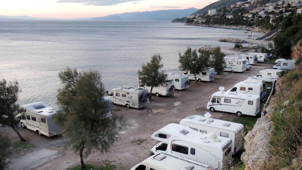 Wohnmobile stehen auf einem Stellplatz am Meer nebeneinander aufgereiht