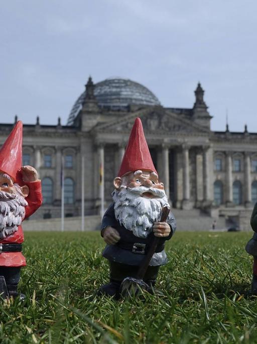 Drei Gartenzwerge stehen auf der Wiese vor dem Reichstag in Berlin.