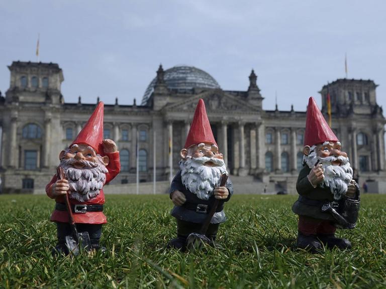 Drei Gartenzwerge stehen auf der Wiese vor dem Reichstag in Berlin.