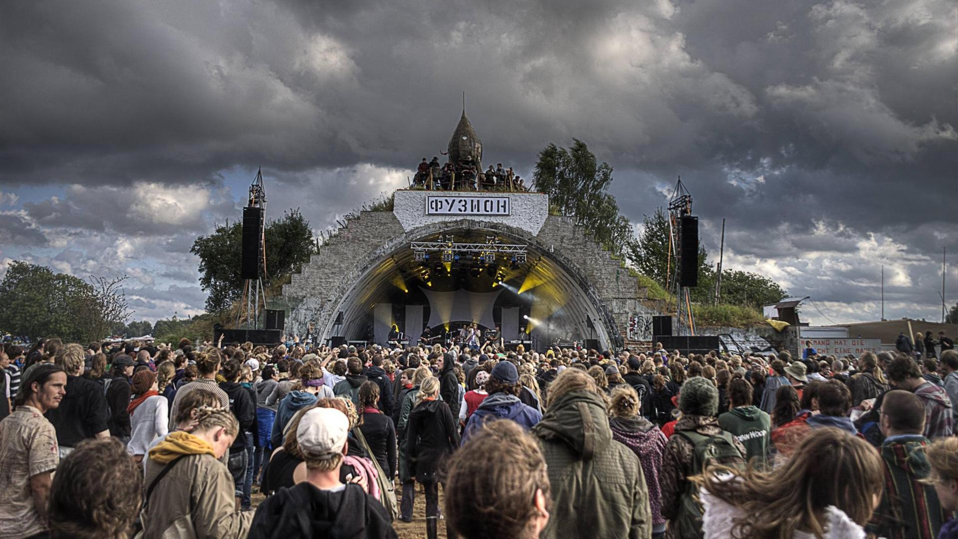 Über der Hauptbühne des Fusion Festivals im mecklenburgischen Lärz sind dunkle Wolken zu sehen. Vor der Bühnen stehen Hunderte Menschen. Über der Hauptbühne des Fusion Festivals im mecklenburgischen Lärz sind dunkle Wolken zu sehen. Vor der Bühnen stehen Hunderte Menschen.