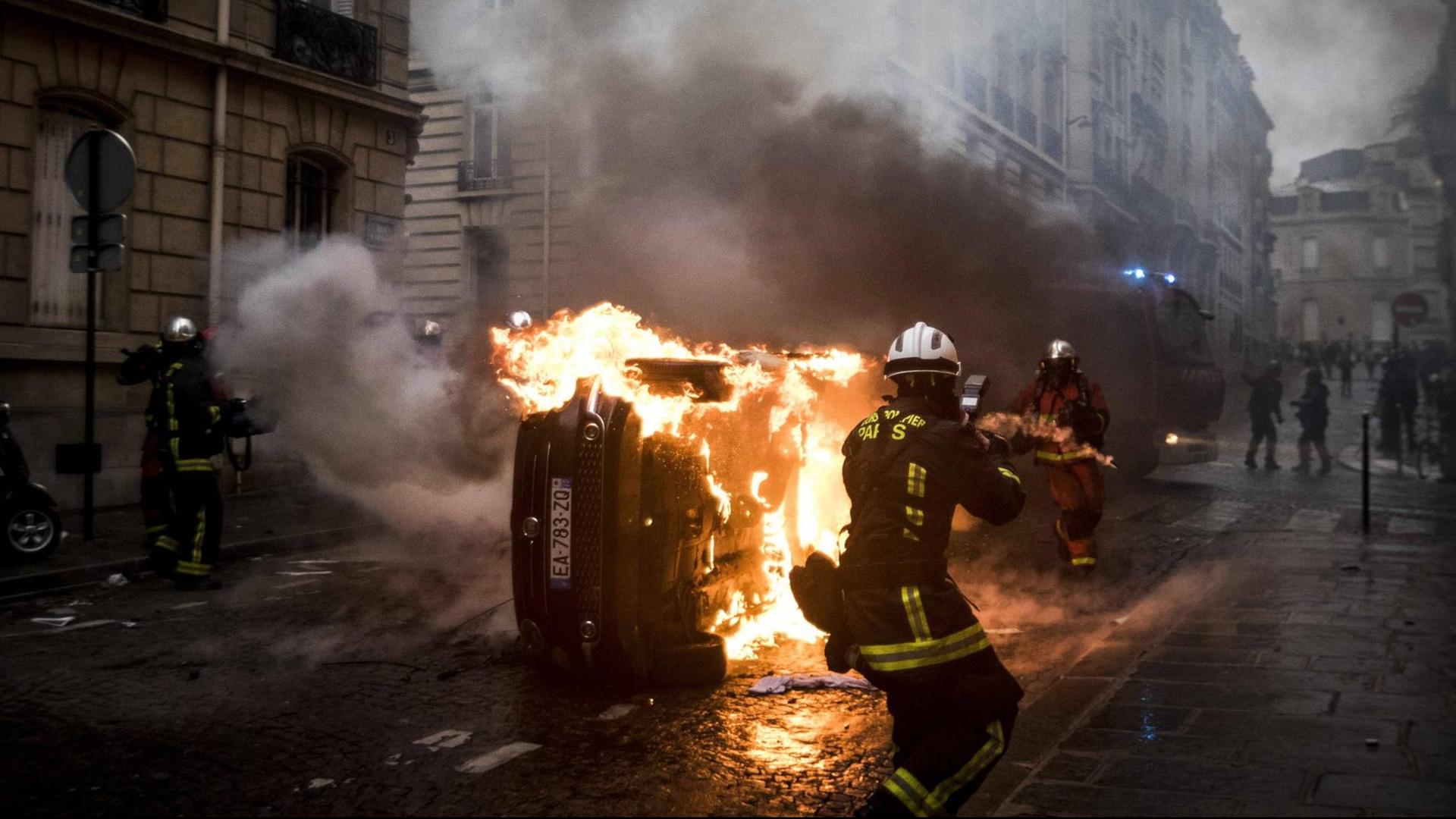 Feuerwehrleute löschen ein brennendes Auto in Paris. Feuerwehrleute löschen ein brennendes Auto in Paris.