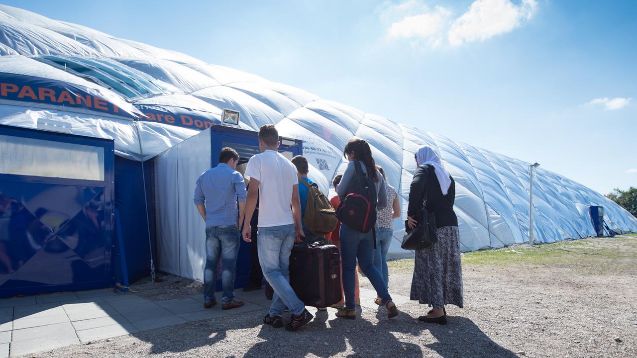 Flüchtlinge in Taufkirchen gehen zu einem von Sicherheitspersonal bewachten Eingang einer Traglufthalle, die als Flüchtlingsunterkunft dient.