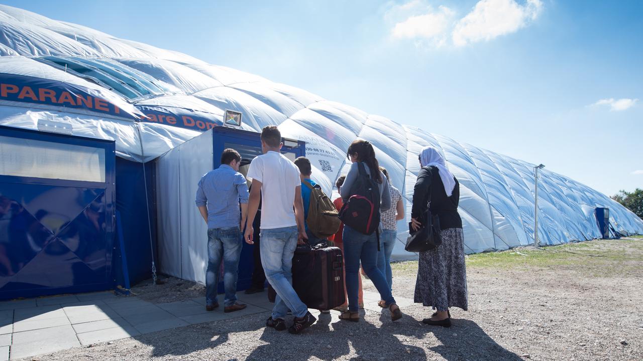 Flüchtlinge in Taufkirchen gehen zu einem von Sicherheitspersonal bewachten Eingang einer Traglufthalle, die als Flüchtlingsunterkunft dient. Flüchtlinge in Taufkirchen gehen zu einem von Sicherheitspersonal bewachten Eingang einer Traglufthalle, die als Flüchtlingsunterkunft dient.