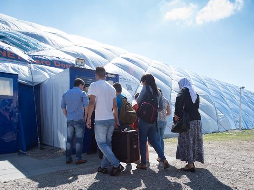 Flüchtlinge in Taufkirchen gehen zu einem von Sicherheitspersonal bewachten Eingang einer Traglufthalle, die als Flüchtlingsunterkunft dient.