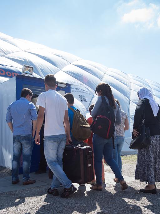 Flüchtlinge in Taufkirchen gehen zu einem von Sicherheitspersonal bewachten Eingang einer Traglufthalle, die als Flüchtlingsunterkunft dient.