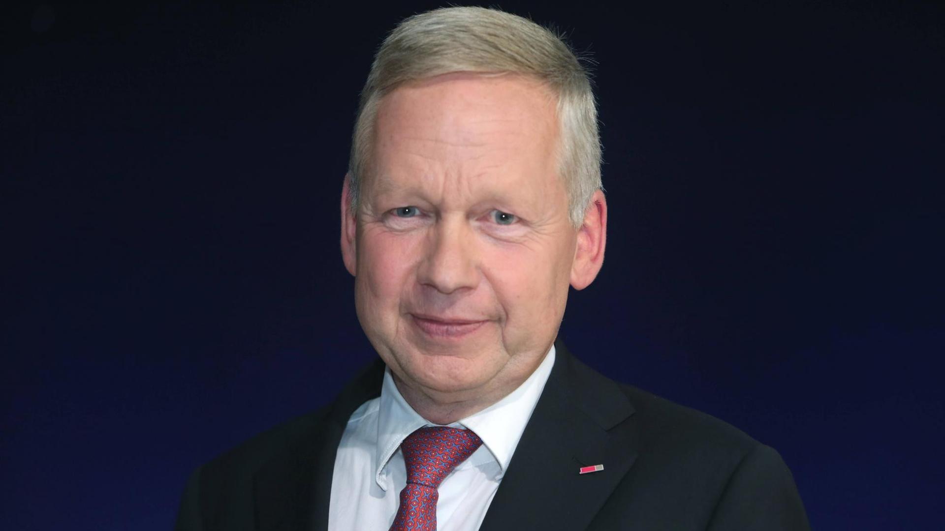 Portraitfoto eines Mannes in mittleren Jahren mit grau-blonden Haaren, der milde lächelt und einen Anzug trägt