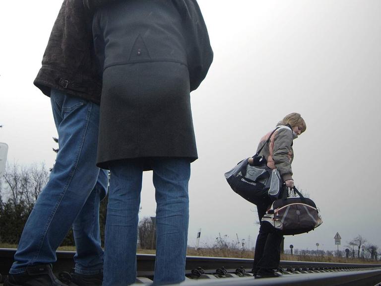 Eltern begleiten ihre Tochter, die ihre Sachen gepackt hat, zum Bahnhof.