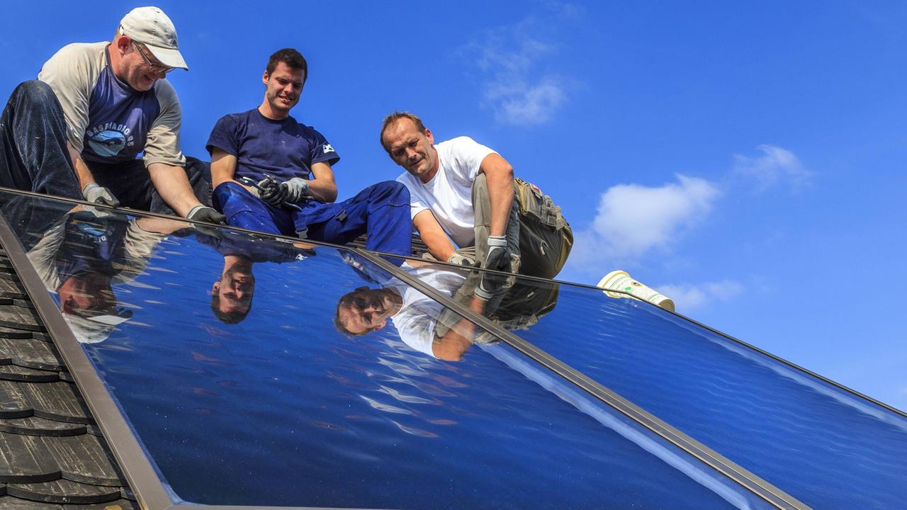 Drei Personen montieren eine Solaranlage auf einem Dach Drei Personen montieren eine Solaranlage auf einem Dach