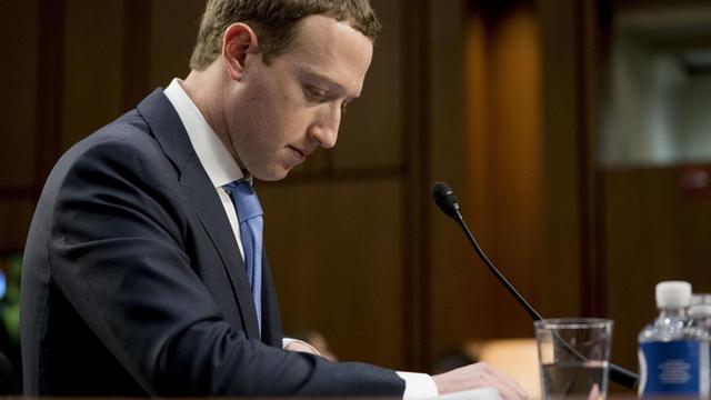 Mark Zuckerberg mit gesenktem Kopf in nachdenklicher Pose während einer öffentlichen Anhörung.