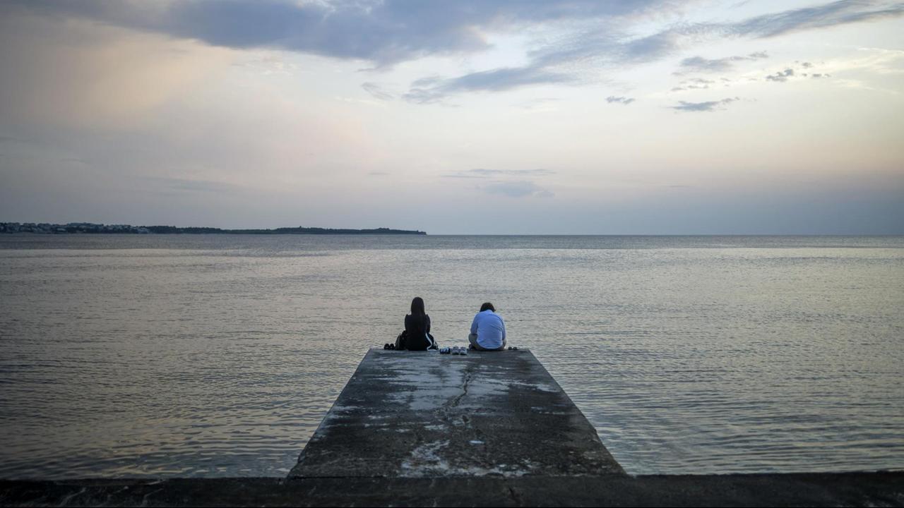 Ein Pärchen sitzt auf einem Pier an der Bucht von Piran in Slowenien Ein Pärchen sitzt auf einem Pier an der Bucht von Piran in Slowenien