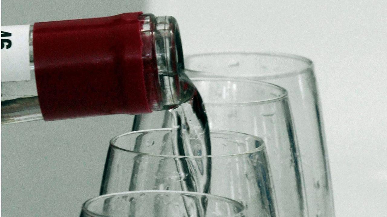 Schnaps wird von einer Flasche in mehrere Gläser gegossen.