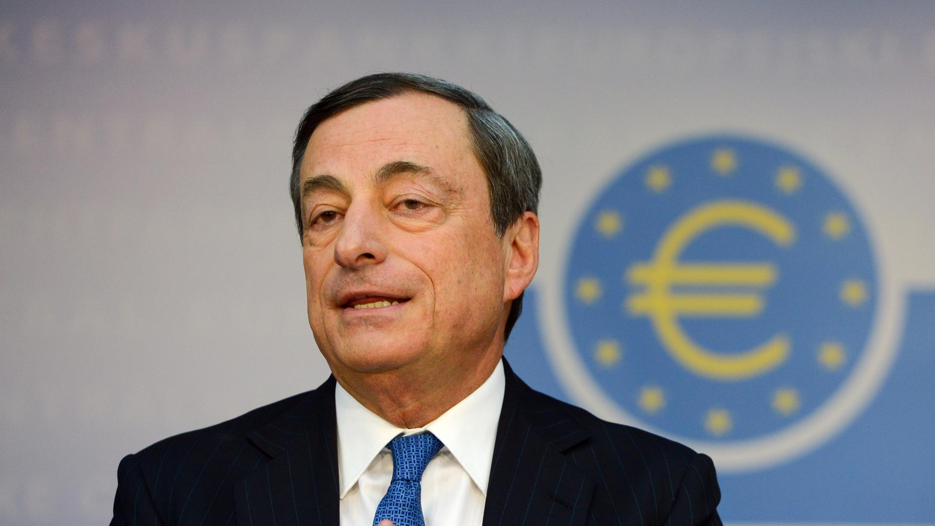 Mario Draghi, Präsident der Europäischen Zentralbank (EZB), im Hintergrund ein Logo mit dem Eurozeichen Mario Draghi, Präsident der Europäischen Zentralbank (EZB), im Hintergrund ein Logo mit dem Eurozeichen