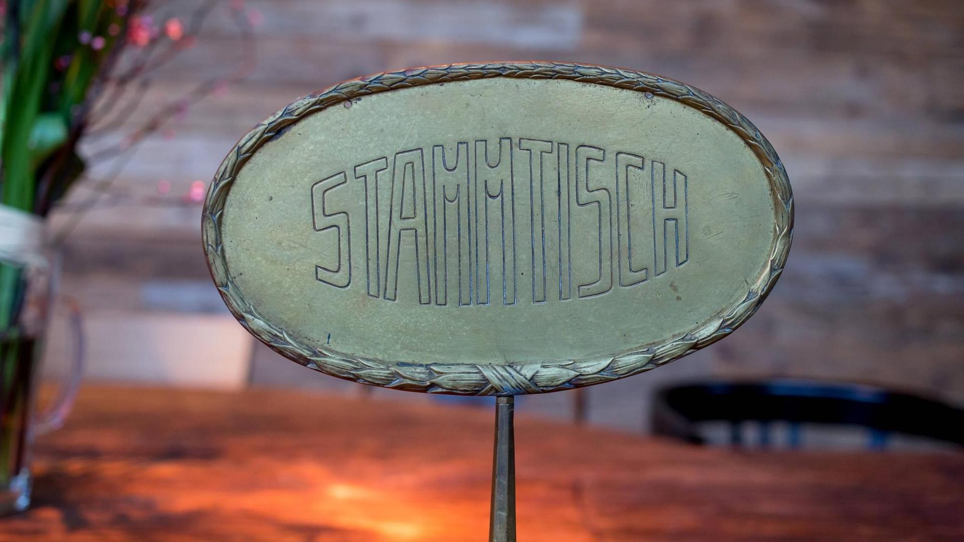 Ein Messingschild auf dem "Stammtisch" steht, im Hintergrund in der Unschärfe Tisch, Stuhl und ein Straß Blumen. Ein Messingschild auf dem "Stammtisch" steht, im Hintergrund in der Unschärfe Tisch, Stuhl und ein Straß Blumen.
