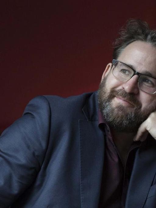 Der Autor und Philosoph Wolfram Eilenberger hat den Kopf auf die linke Hand gestützt und schaut nachdenklich schmunzelnd in die Höhe.