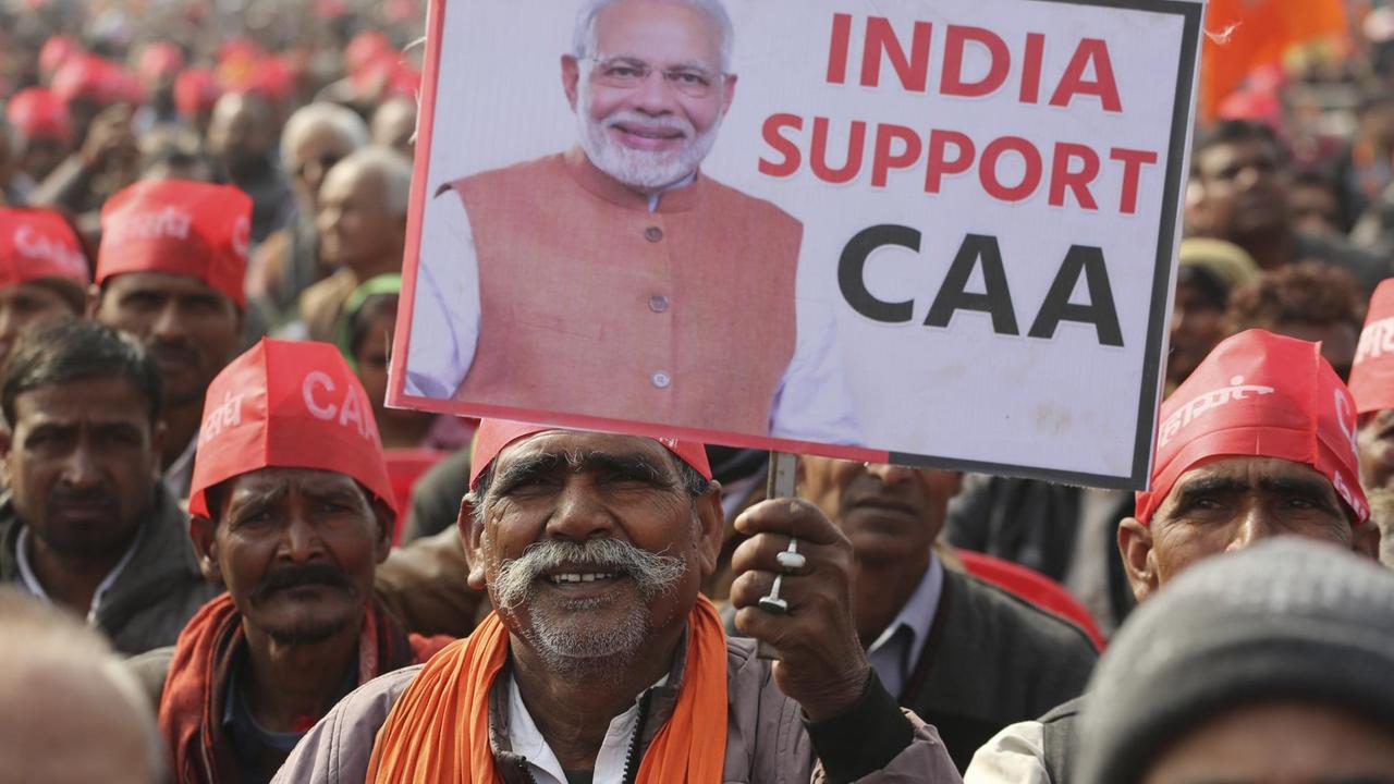 Ein Anhänger von der Regierungspartei BJP hält während einer Demonstration ein Schild mit dem Bild des Premiers Narendra Modi und dem Schriftzug "India support CAA" hoch. Ein Anhänger von der Regierungspartei BJP hält während einer Demonstration ein Schild mit dem Bild des Premiers Narendra Modi und dem Schriftzug "India support CAA" hoch.