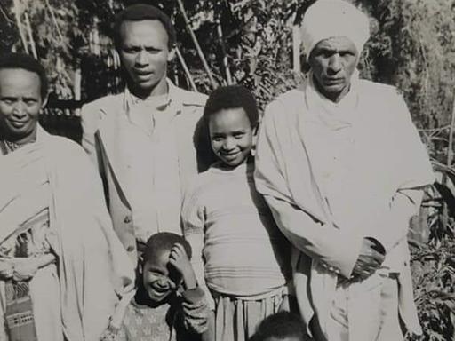 Die Schwarzweißfotografie zeigt eine schwarze Familie. Zu sehen sind Mutter, Vater (mit weißer Kopfbedeckung) und drei Söhne.