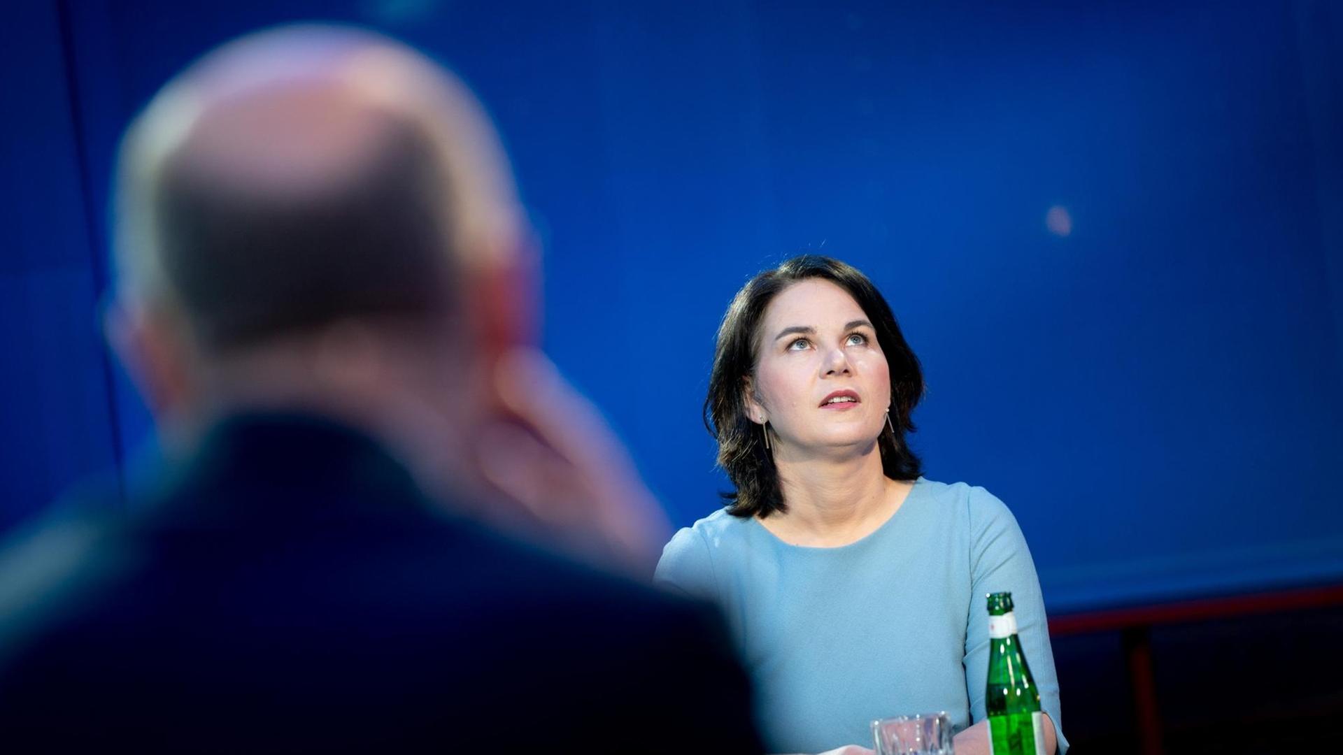 Die grüne Kanzlerkandidatin Annalena Baerbock steht an einem Tisch und schaut nach oben, im Vordergrund unscharf und von hinten Olaf Scholz, Kanzlerkandidat der SPD. Die grüne Kanzlerkandidatin Annalena Baerbock steht an einem Tisch und schaut nach oben, im Vordergrund unscharf und von hinten Olaf Scholz, Kanzlerkandidat der SPD.