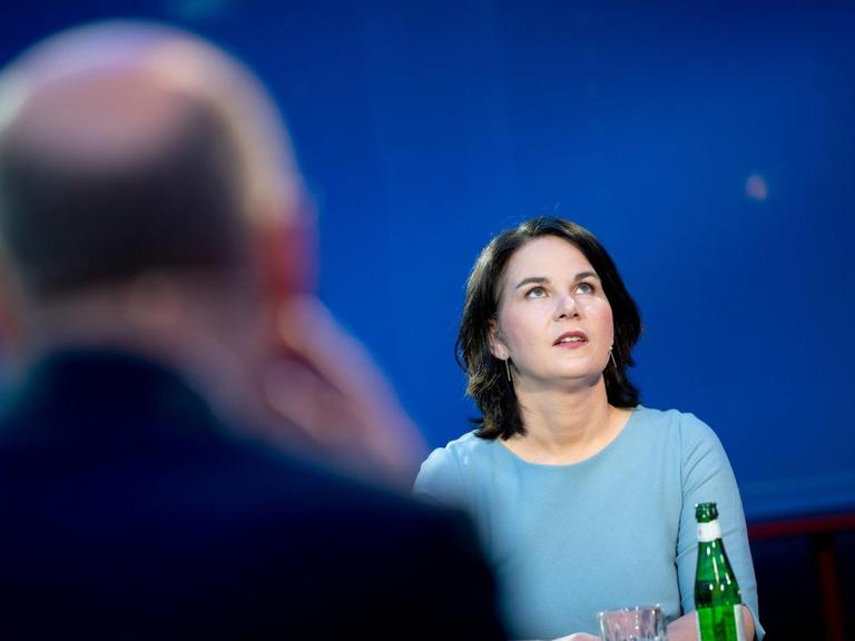 Die grüne Kanzlerkandidatin Annalena Baerbock steht an einem Tisch und schaut nach oben, im Vordergrund unscharf und von hinten Olaf Scholz, Kanzlerkandidat der SPD.