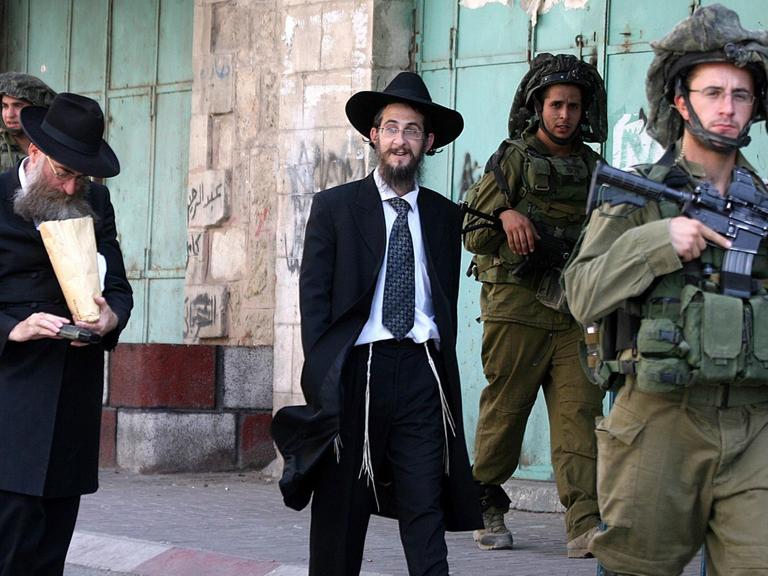 Israelische Siedler laufen bewacht von Soldaten durch eine Straße in Hebron, die nur ihnen zugänglich ist.