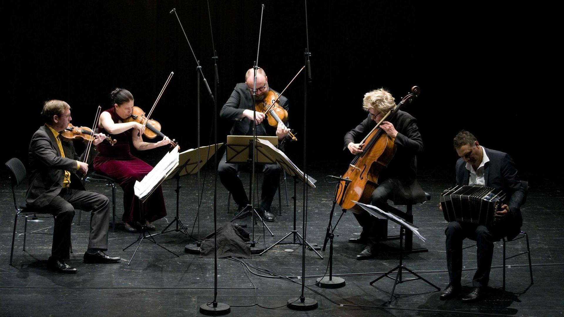 Ein Streichquarett und ein Bandoneonist im Zusammenspiel auf einer Bühne. Ein Streichquarett und ein Bandoneonist im Zusammenspiel auf einer Bühne.