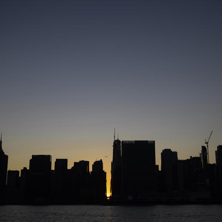 Hinter den unbeleuchteten Wolkenkratzern von Manhattan geht die Sonne unter - Blick vom Wasser aus gesehen.