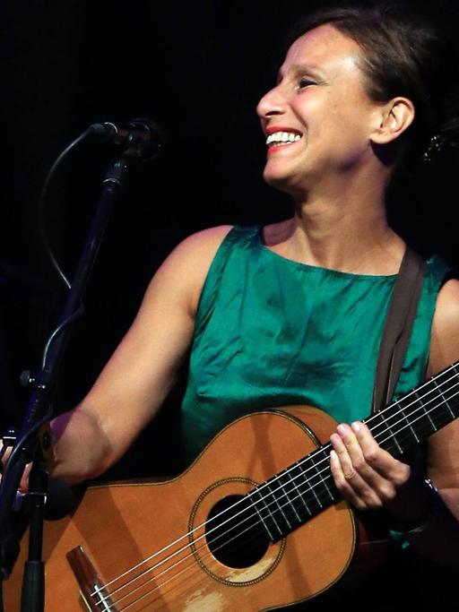 Die italienische Sängerin und Songwriterin Etta Scollo beim Rheingau Musikfestival 2015. Sie trägt ein grünes Kleid und hält eine Gitarre im Arm.