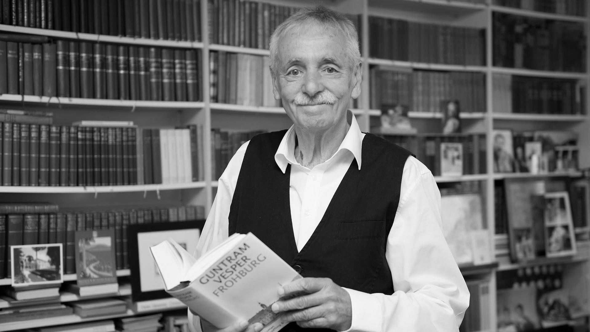 Der Schriftsteller Guntram Vesper steht vor einem Bücherregal und hält ein Buch in der Hand